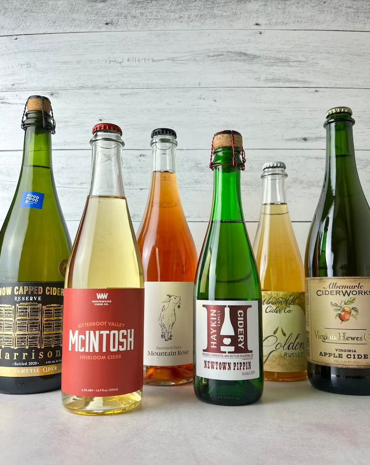 6 bottles of cider, from left to right: Snow Capped Harrison, Whitewood McIntosh, Bauman's Mountain Rose, Union Hill Golden Russet, and Albemarle Virginia Hewe's Crab