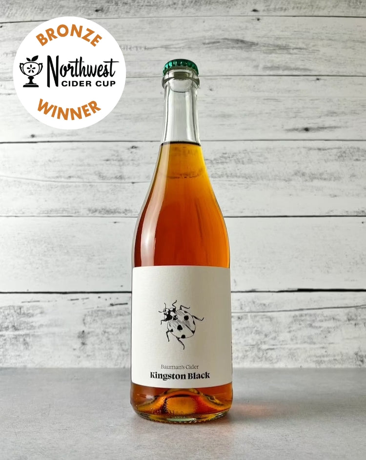 Photo of A bottle of Bauman's Cider Kingston Black single-varietal cider with a label showing a black and white lady-bug drawing. There is a Bronze Northwest Cider Cup award badge displayed in the top left corner.