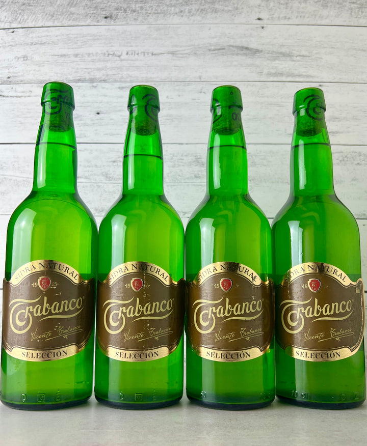 Photo of Four green bottles of Trabanco cider on a light grey surface