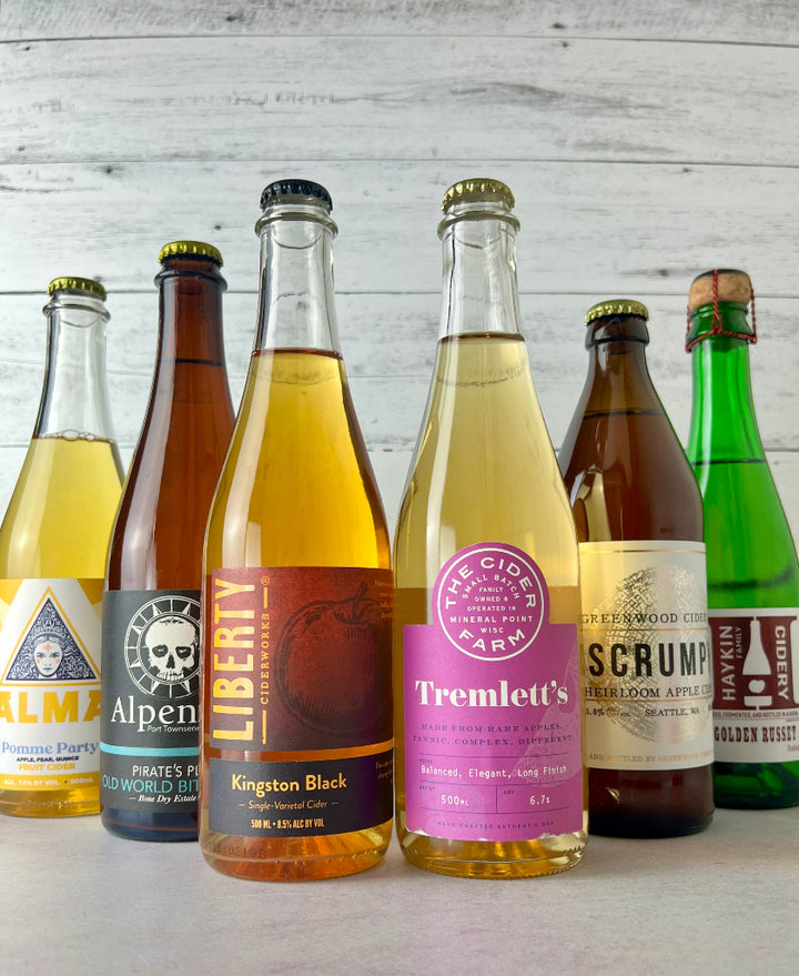 Photo of six bottles of 500 and 375 mL bottles, including Alma Pomme Party, Alpenfire Pirate's Plank, Haykin Cidery Golden Russet,  Liberty Ciderworks Kingston Black, and Greenwood Scrumpy