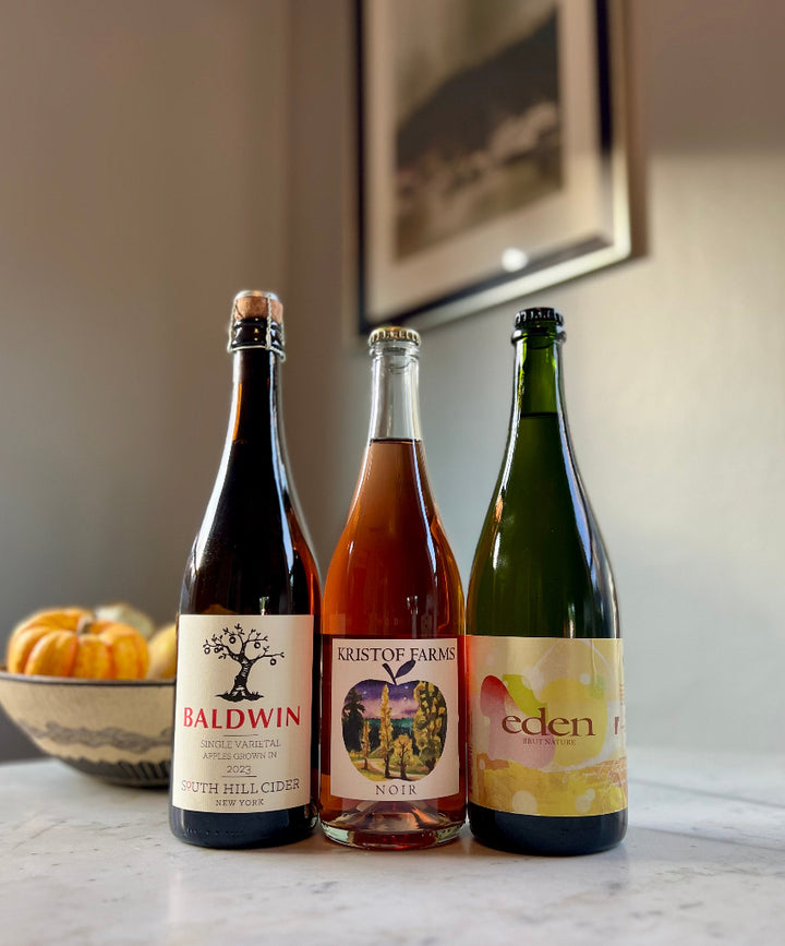 Photo of 3-bottles of cider, from left to right: South Hill Cider Baldwin, Kristof Farms Noir, Eden Brut Nature