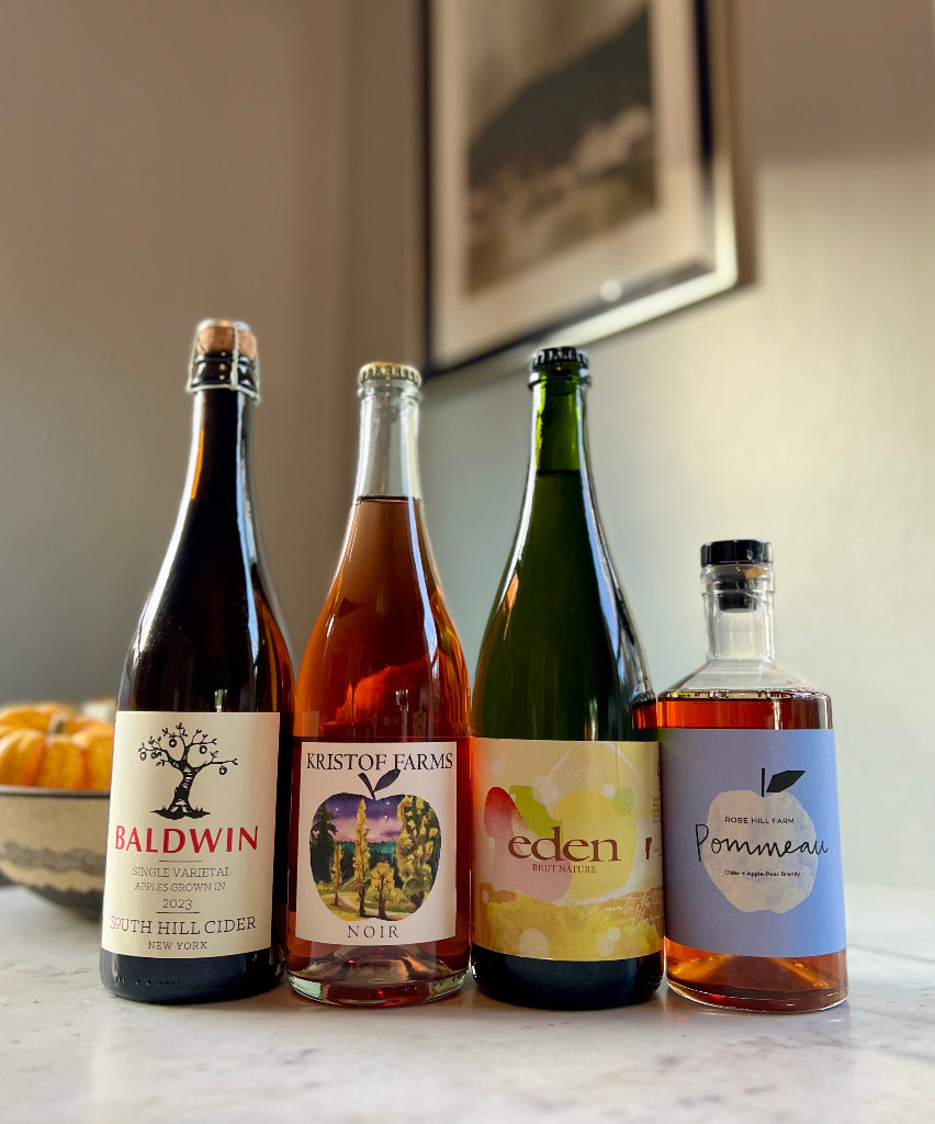 Photo of 4-bottles of cider, from left to right: South Hill Cider Baldwin, Kristof Farms Noir, Eden Brut Nature, Rose Hill Farm Pommeau