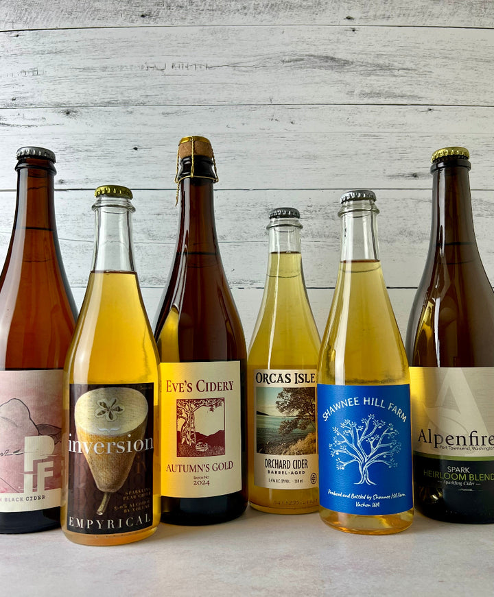 Photo of 6 bottles of cider, from left to right: PIF Cider, Empyrical Cider, Eve's Cidery, Orcas Isle Cider, Shawnee Hill Farm, and Alpenfire Cider