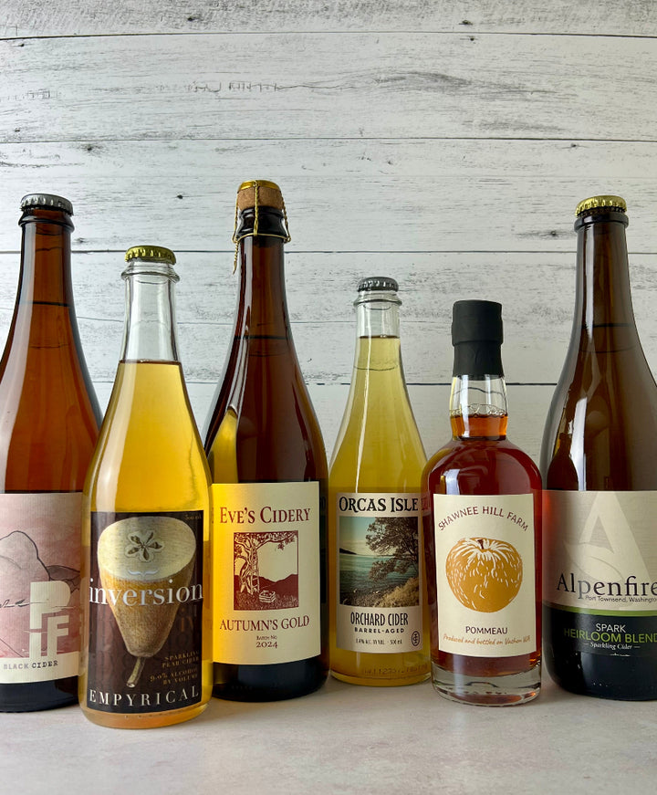 Photo of 6 bottles of cider, from left to right: PIF Cider, Empyrical Cider, Eve's Cidery, Orcas Isle Cider, Shawnee Hill Farm Pommeau, and Alpenfire Cider