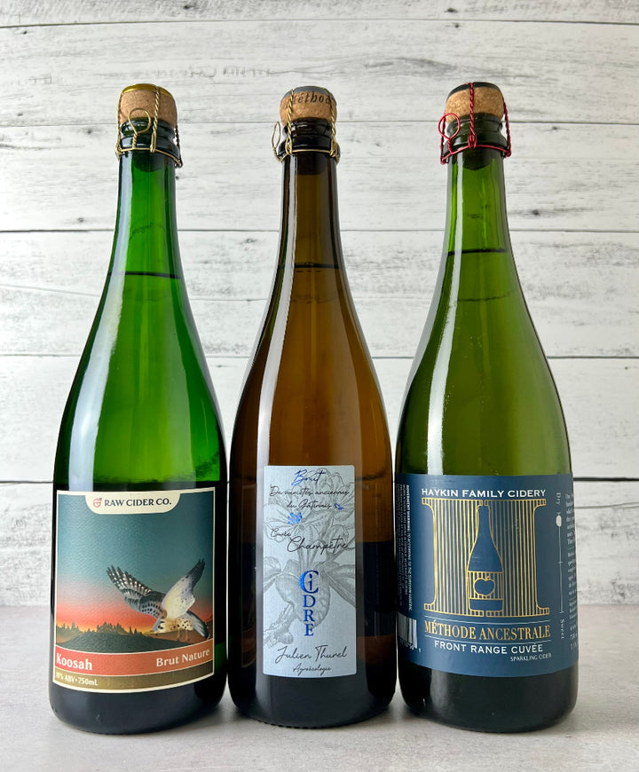 Photo of 3 bottles of cork and caged sparkling ciders: RAW Koosah Brut Nature, Julien Thurel Cidre Champêtre Cidre Extra Brut, and Haykin Family Cider Front Range Cuvee