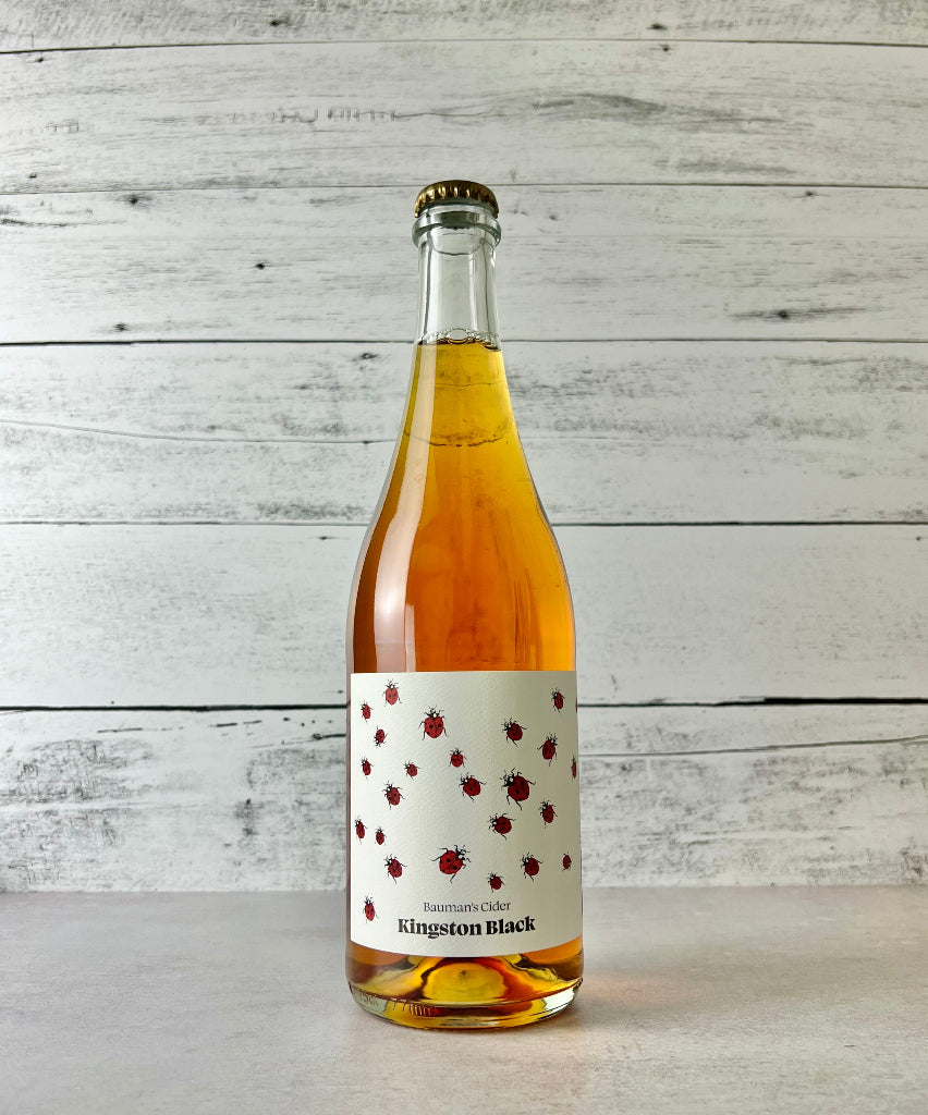 Photo of a 750 mL bottle of Bauman's Kingston Black Cider with a white label and drawing of red and black lady bugs.