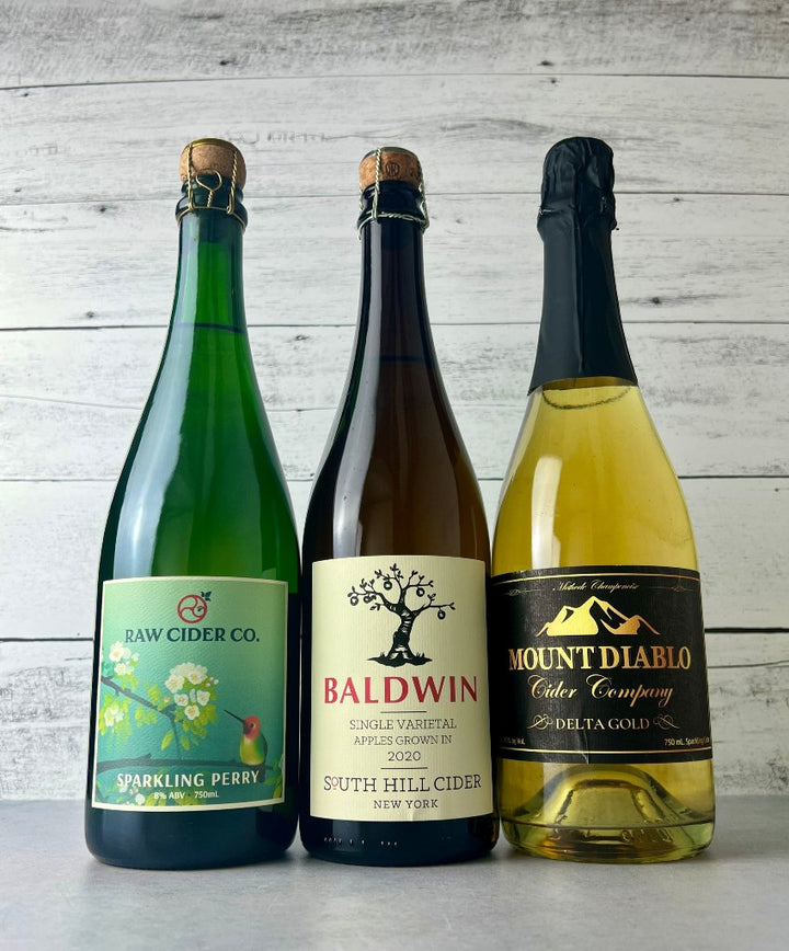 Three 750 mL bottles of cider with cork and cage: Raw Cider Sparkling Perry, South Hill Cider Baldwin, Mount Diablo Cider Delta Gold