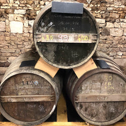 Three wood barrels stacked like a pyramid with two on bottom and one on top. Stone wall in background
