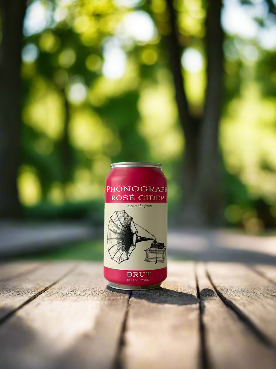 12 oz pink can of Phonograph Rosé Cider Brut on a picnic table with trees in the background