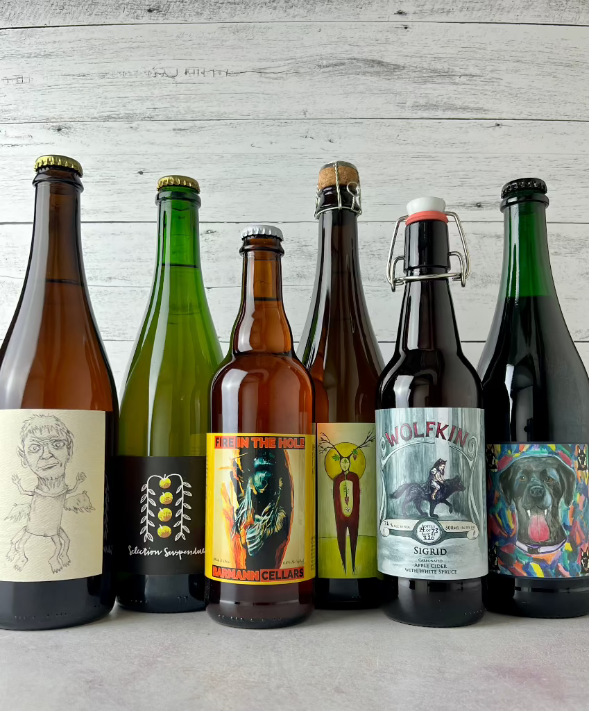 6 bottles of cider, from left to right: Eve's Dabinett, Rose Hill Farm Selection Suspendue, Barmann Cellars Fire in the Hole, South Hill Cider Coferment, Wofkin Sigrid, Durham Henri & Luci