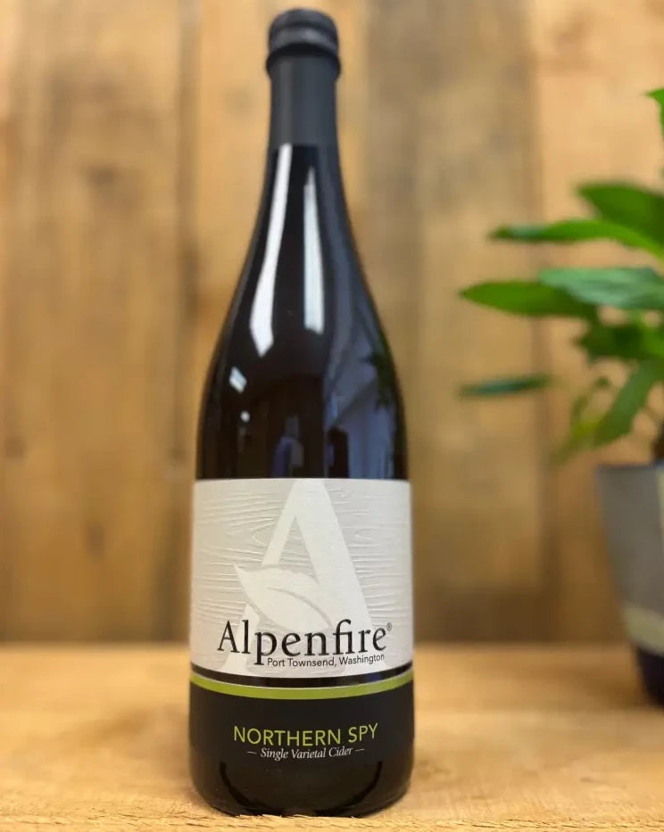 Bottle of Alpenfire Northern Spy cider on wood table with houseplant in foreground and a wood backdrop